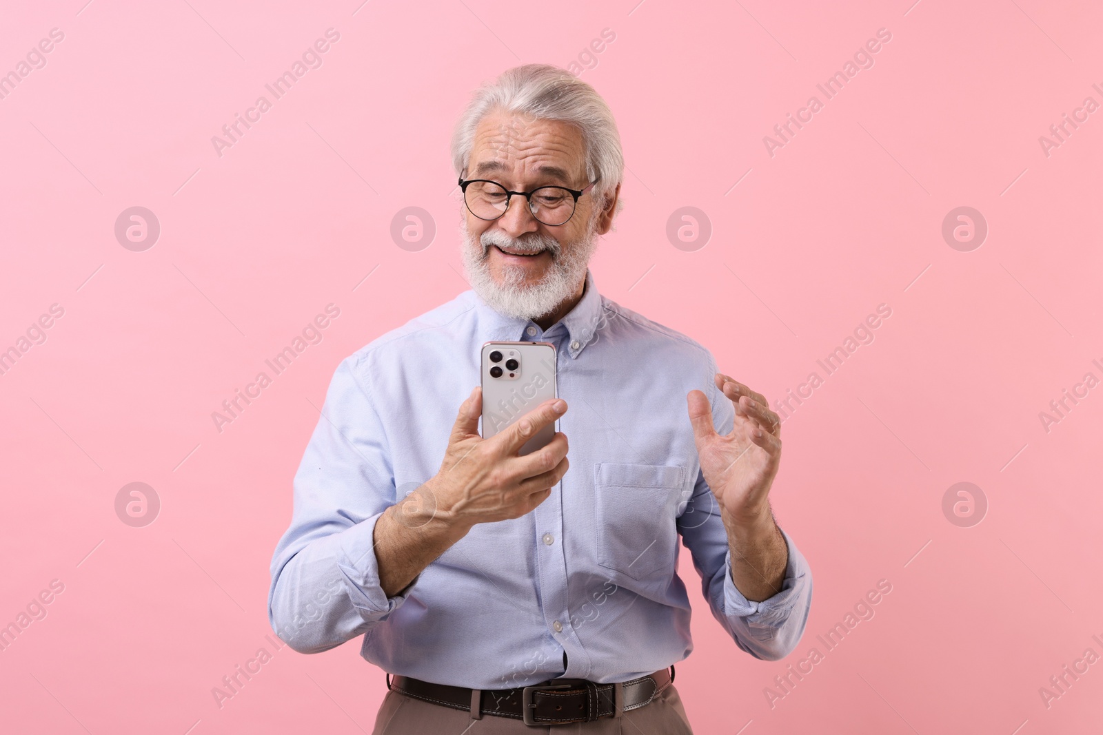 Photo of Portrait of stylish grandpa with glasses using smartphone on pink background