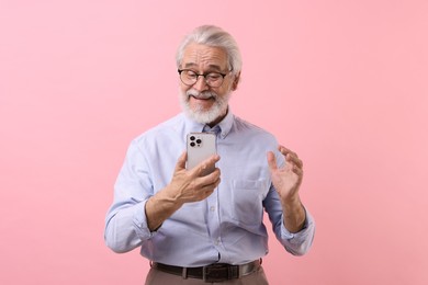 Portrait of stylish grandpa with glasses using smartphone on pink background
