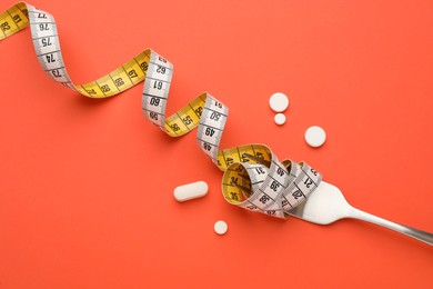 Photo of Weight loss pills, measuring tape and fork on coral background, flat lay