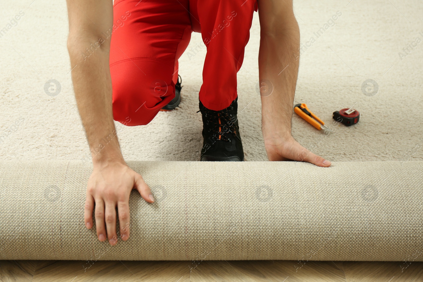 Photo of Worker rolling out new carpet flooring indoors, closeup