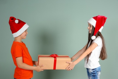 Photo of Cute little children in Santa hats with Christmas gift box on color background