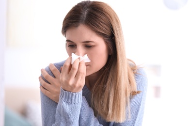 Sad woman with tissue suffering from cold on blurred background