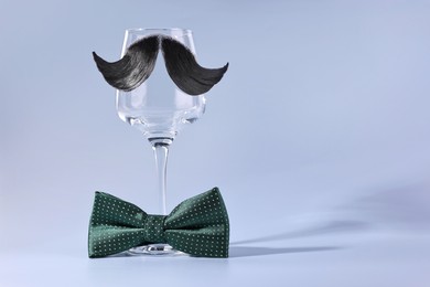 Man's face made of artificial mustache, bow tie and wine glass on light blue background. Space for text