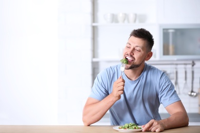 Portrait of happy man eating broccoli salad in kitchen