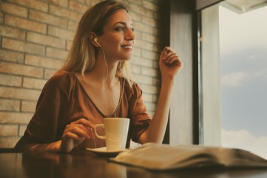 Image of Woman with earphones and cup of coffee at table in cafe
