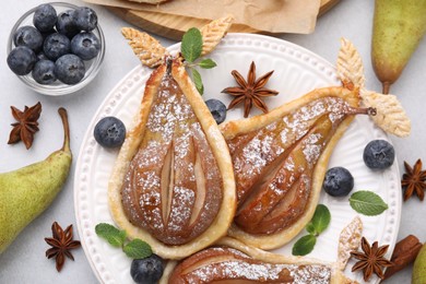 Photo of Delicious pears baked in puff pastry with powdered sugar served on light grey table, flat lay