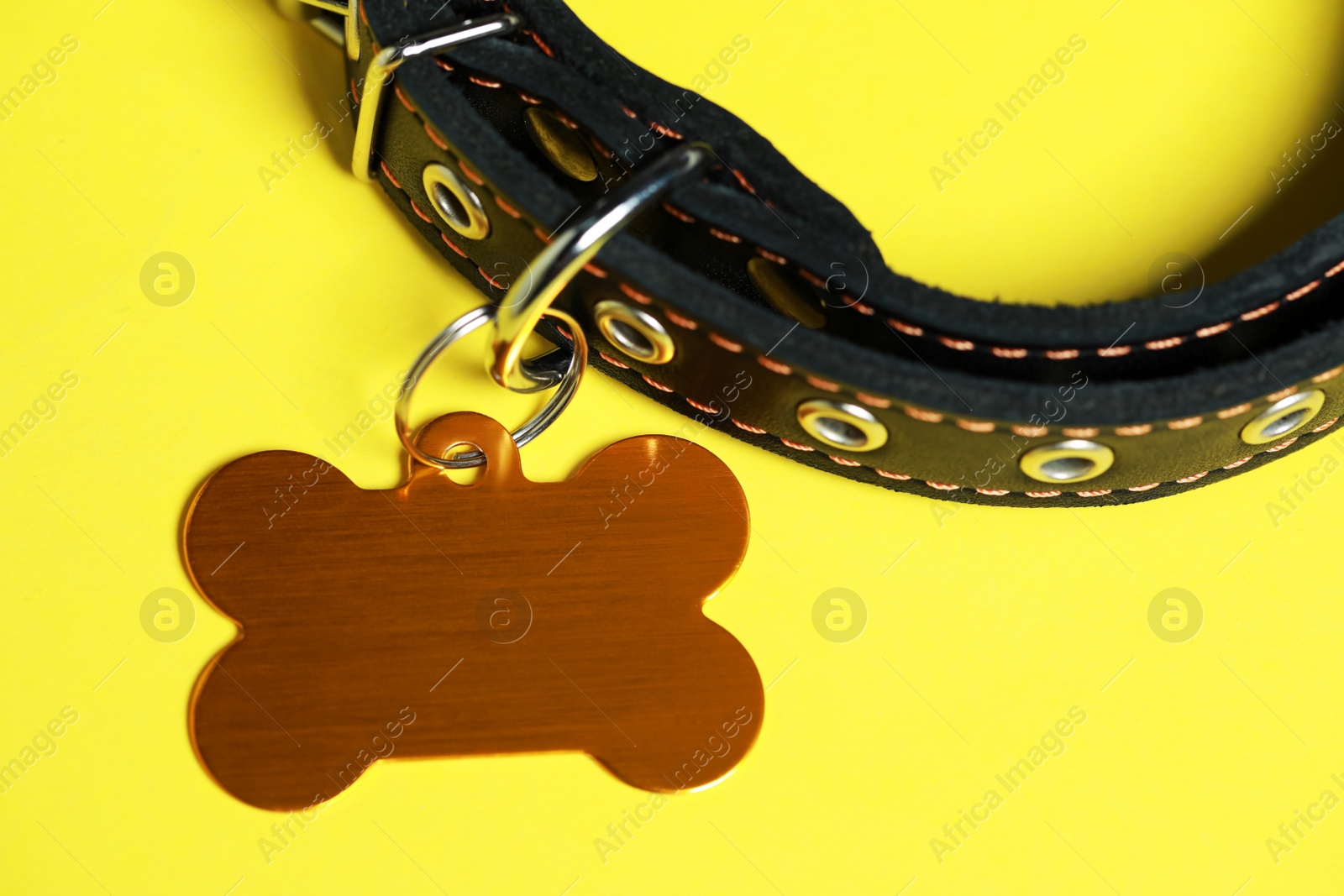 Photo of Black leather dog collar with golden tag in shape of bone on yellow background, closeup. Space for text