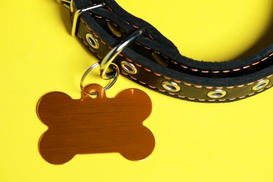 Photo of Black leather dog collar with golden tag in shape of bone on yellow background, closeup. Space for text