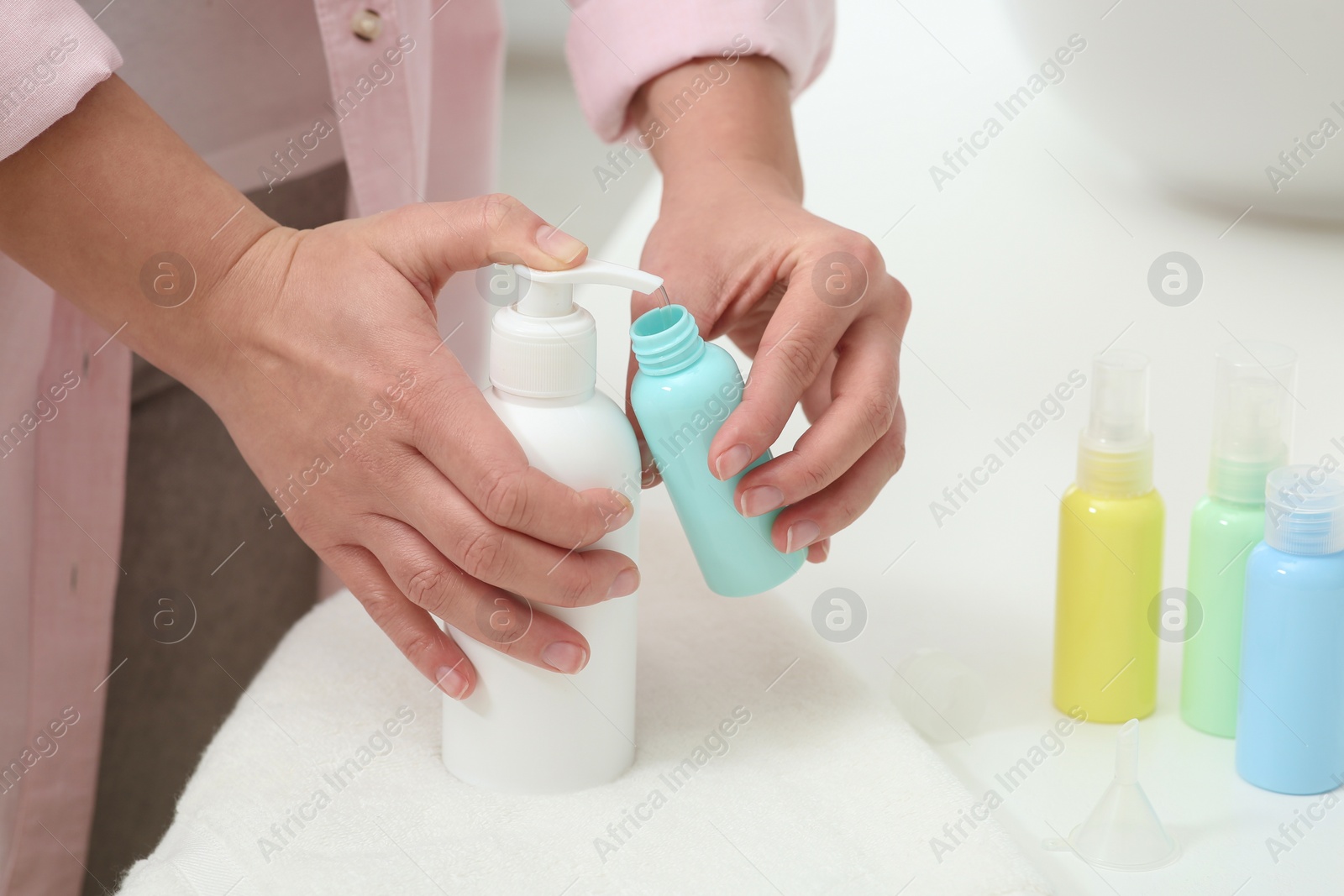 Photo of Woman pouring cosmetic product into plastic bottle at white countertop, closeup and space for text. Bath accessories