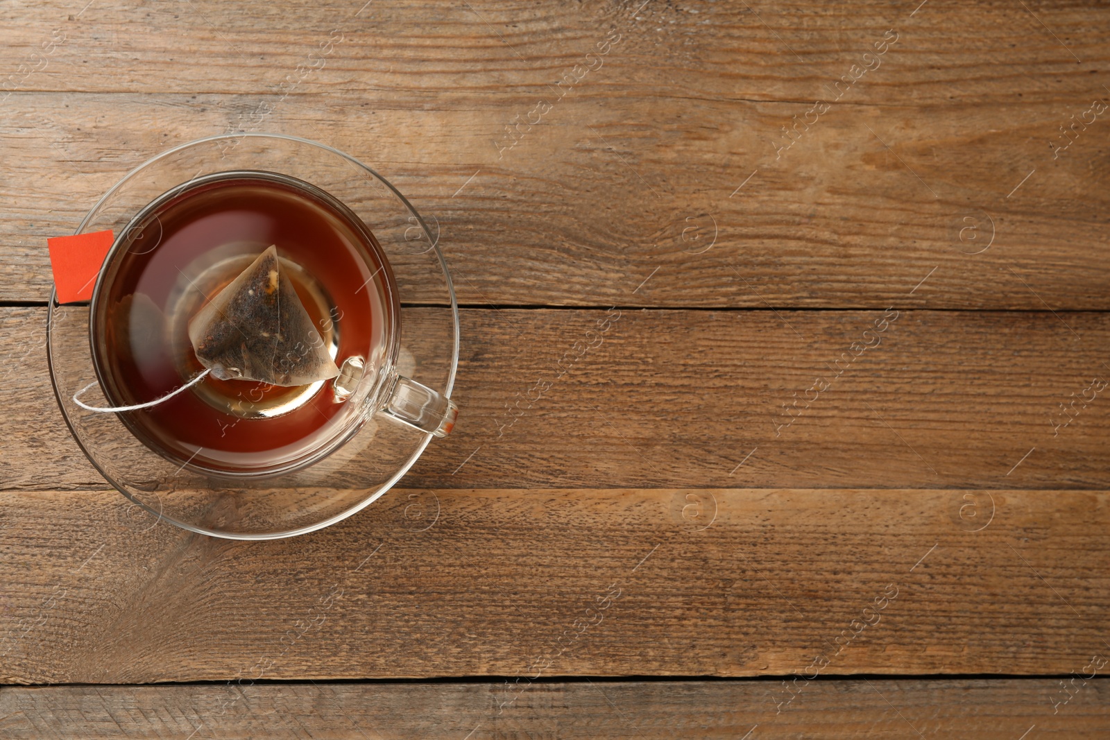 Photo of Tea bag in glass cup of hot water on wooden table, top view. Space for text