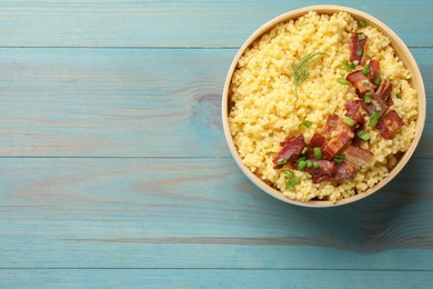 Tasty millet porridge with bacon, green onion and dill in bowl on light blue wooden table, top view. Space for text