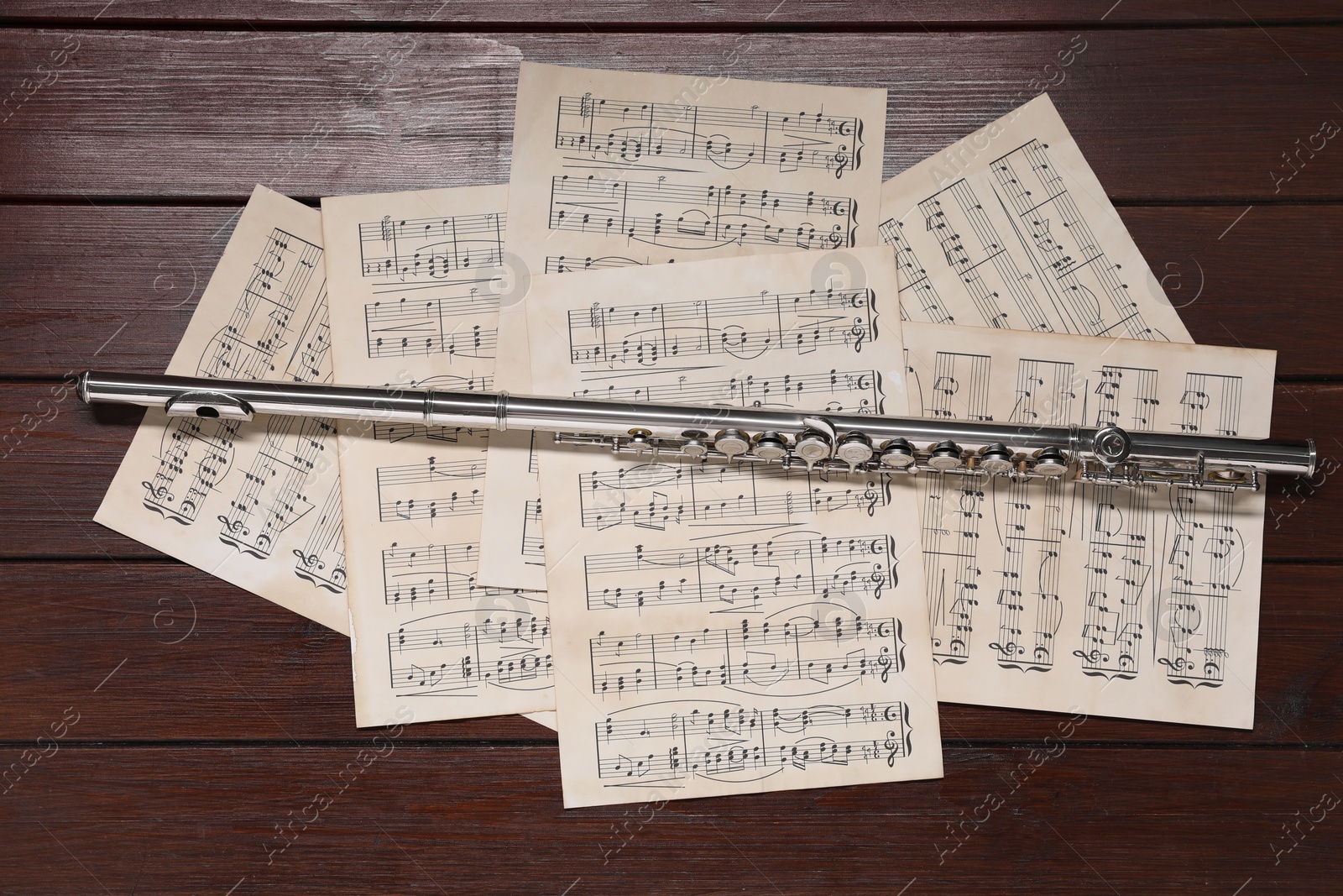 Photo of Sheets with musical notes and flute on wooden table, flat lay