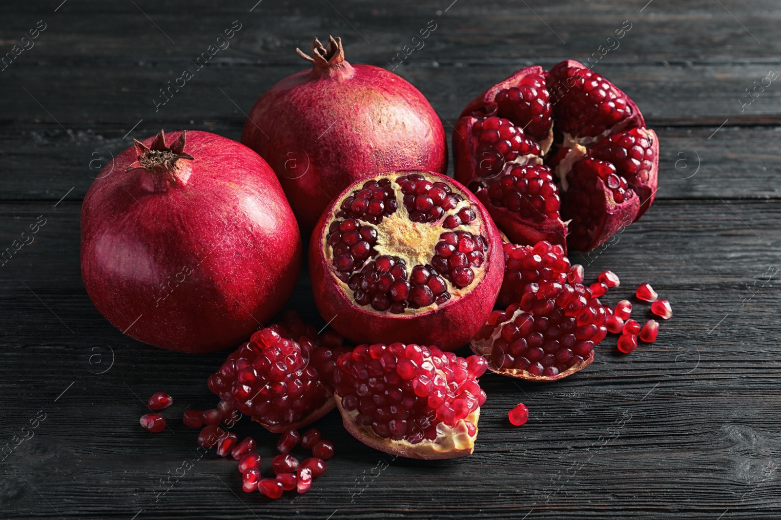 Photo of Ripe pomegranates and seeds on wooden background