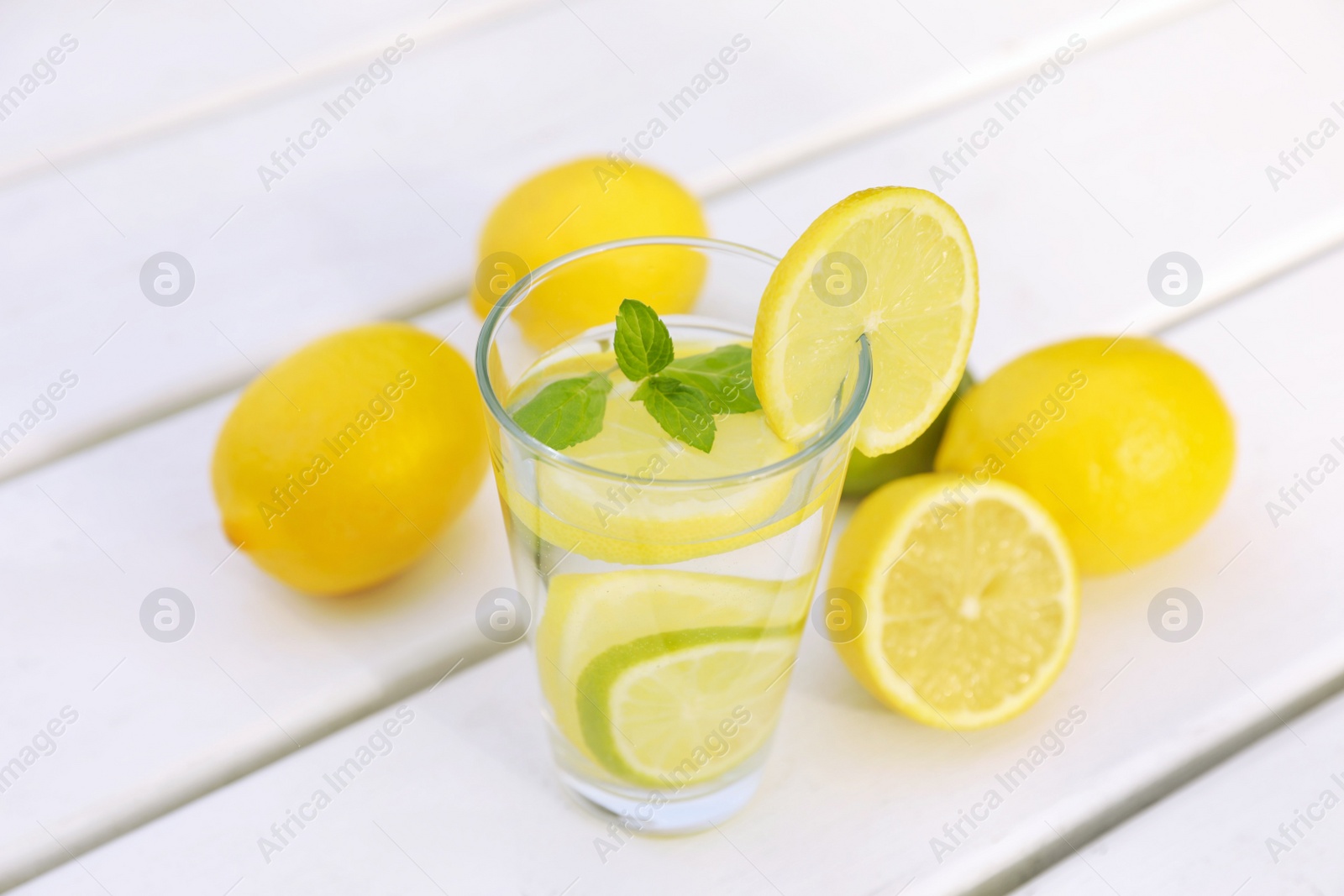 Photo of Glass of water with lemons and mint on white wooden table