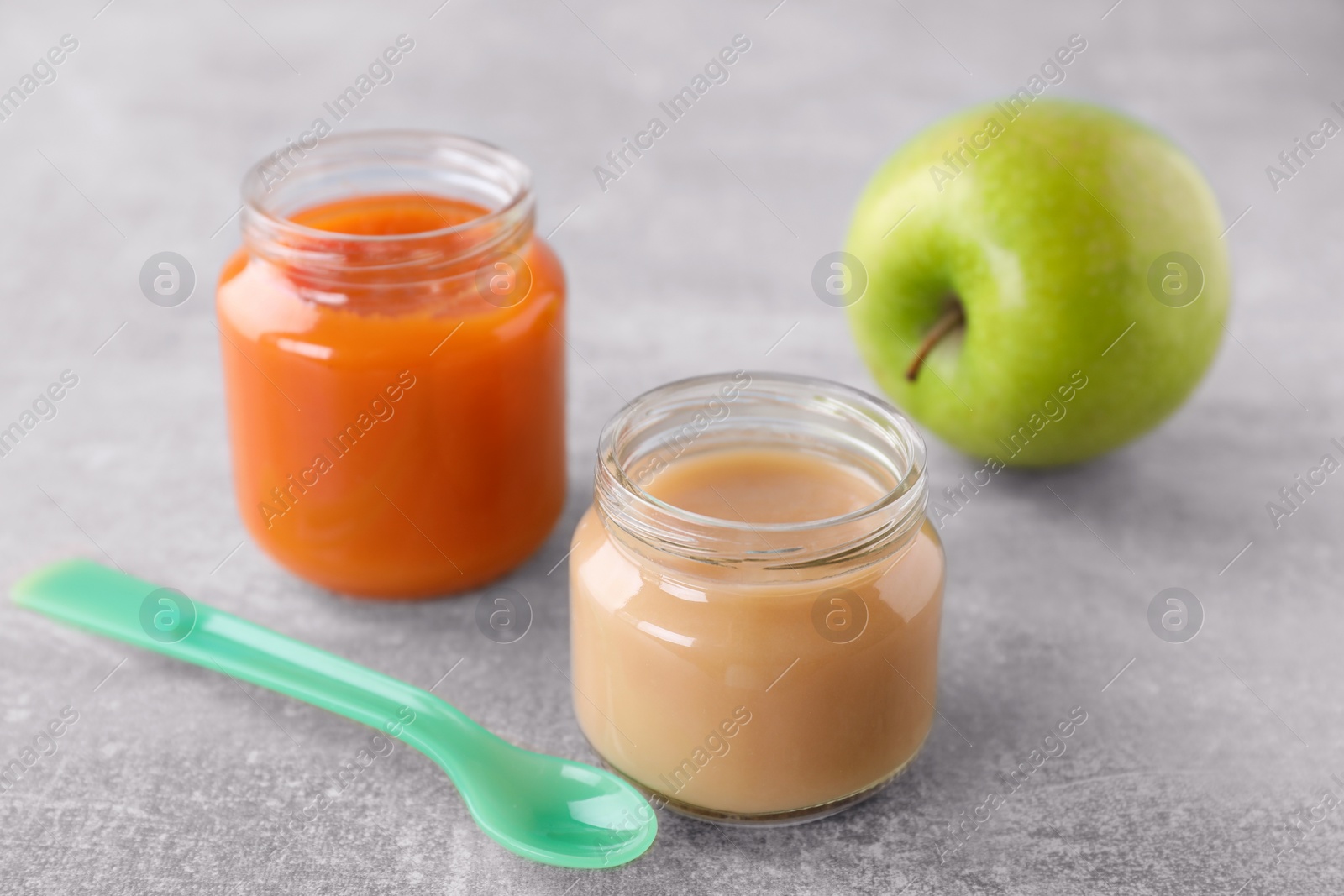 Photo of Jars with healthy baby food, apple and spoon on light grey table