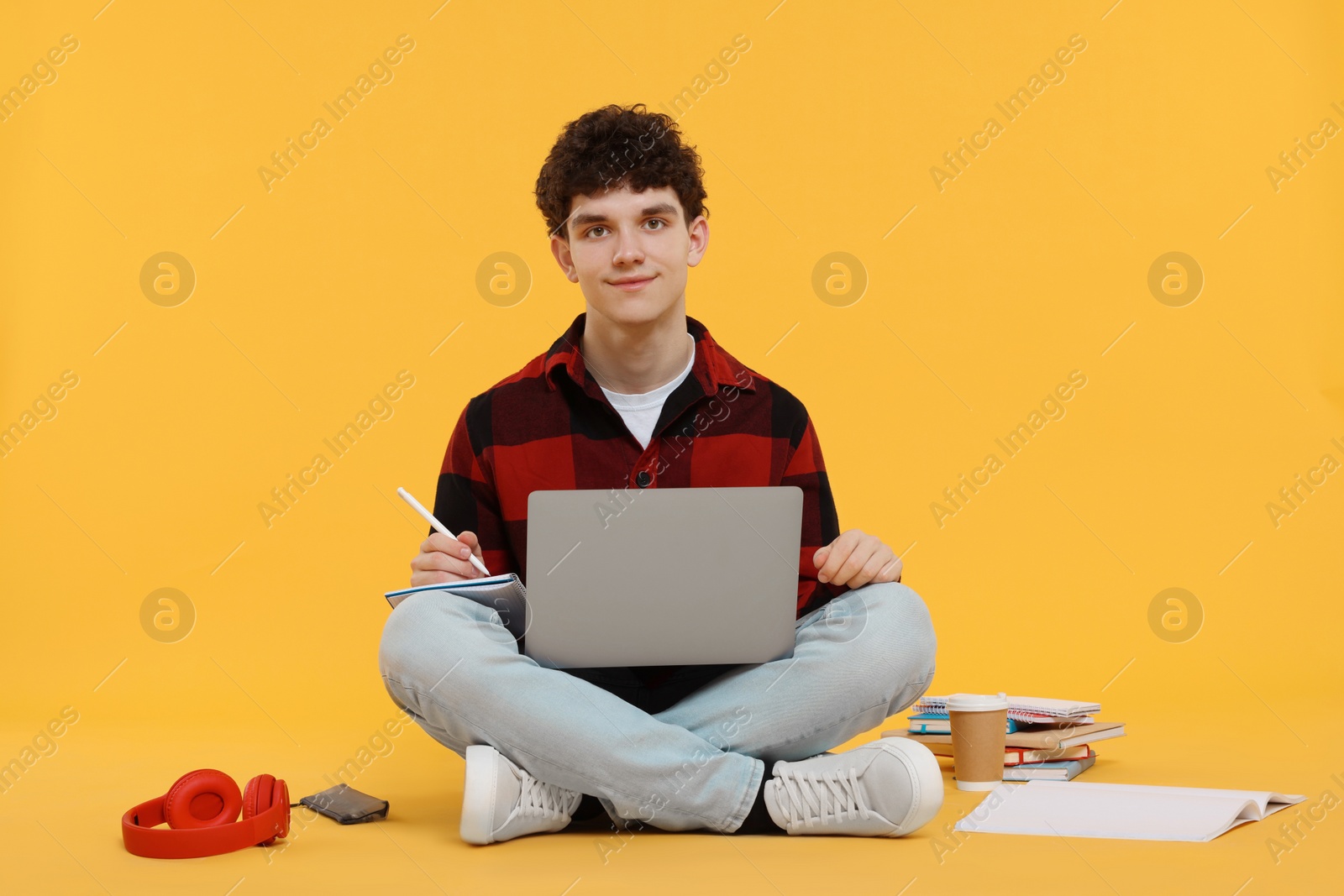 Photo of Portrait of student with laptop and stationery sitting on orange background