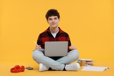 Portrait of student with laptop and stationery sitting on orange background