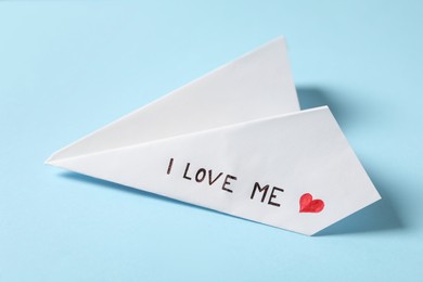 Photo of Paper plane with phrase I Love Me on light blue background