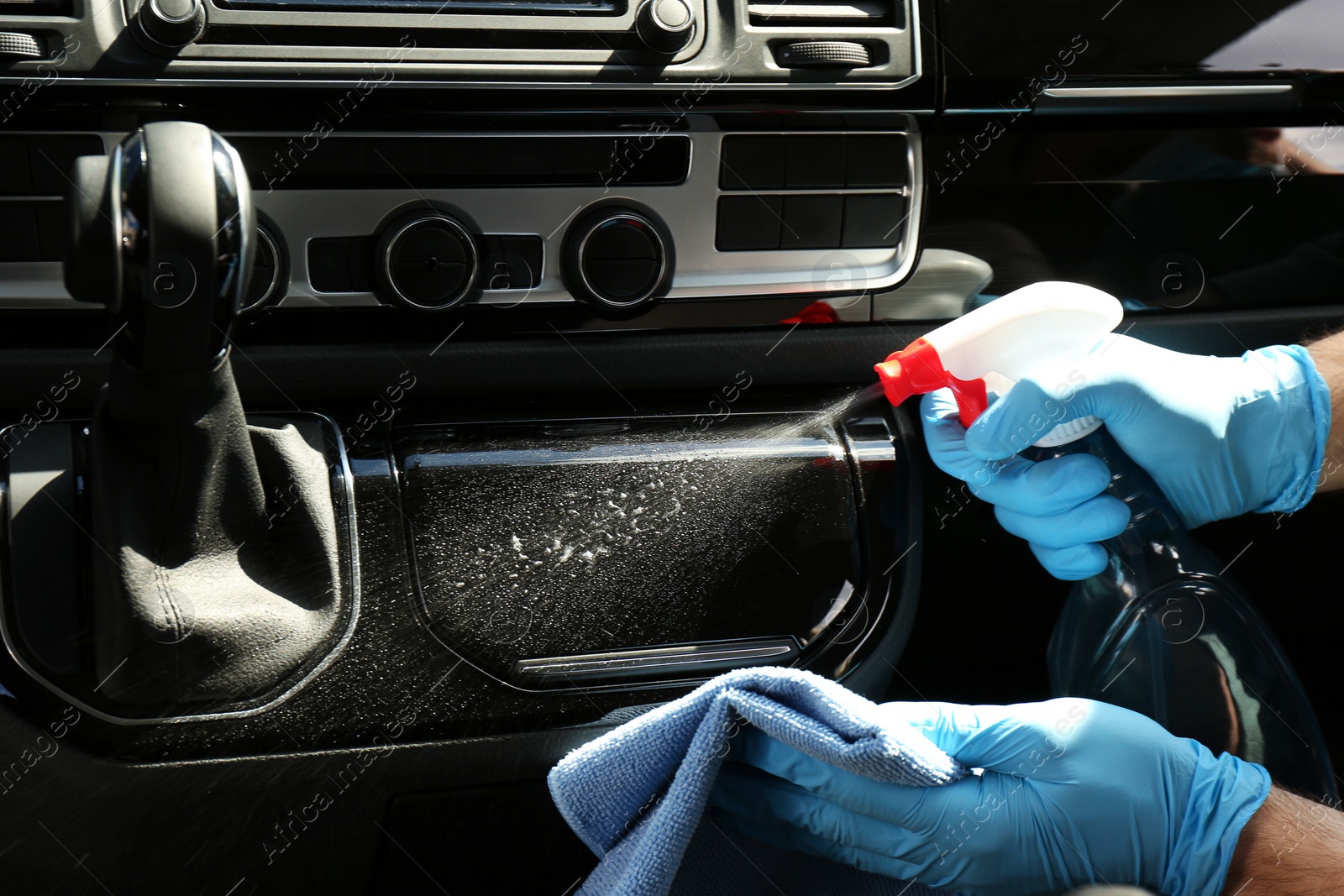 Photo of Man in gloves cleaning car dashboard with disinfectant spray and rag, closeup. Preventive measure during coronavirus pandemic