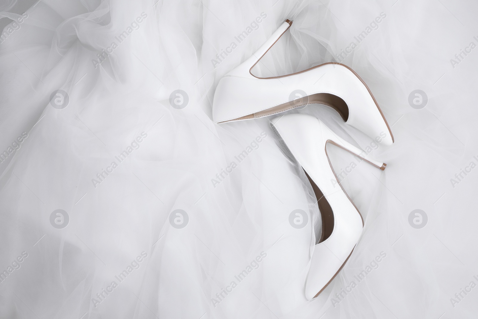 Photo of Pair of wedding high heel shoes on white veil, flat lay