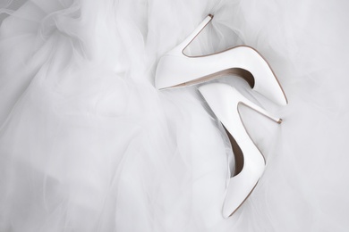 Photo of Pair of wedding high heel shoes on white veil, flat lay