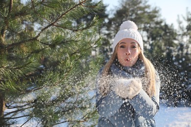 Woman blowing snow from hands in winter forest, space for text