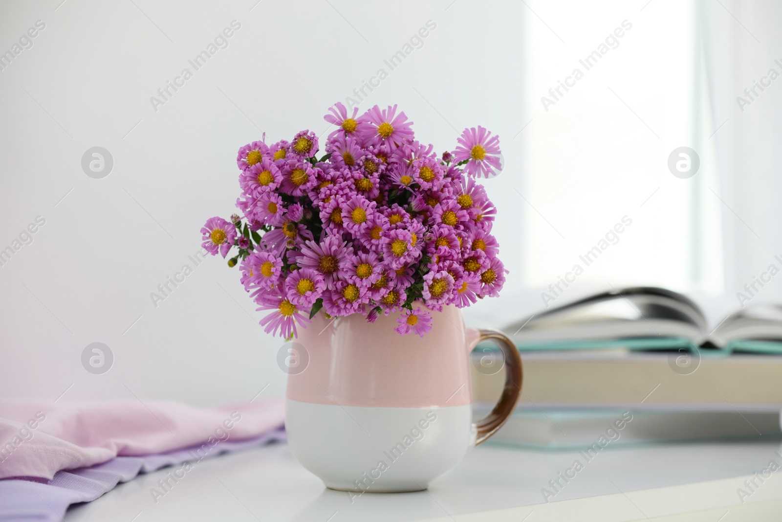 Photo of Cup with beautiful flowers on white table in light room