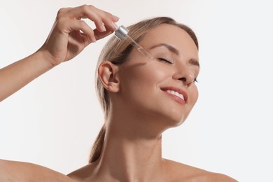 Beautiful woman applying cosmetic serum onto her face on white background