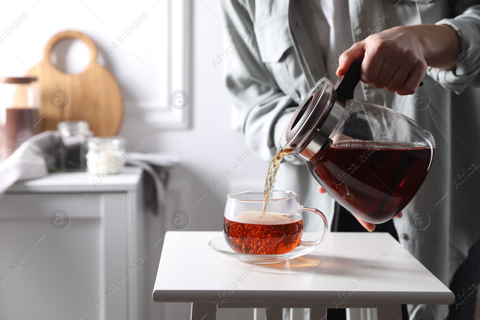 Photo of Woman pouring hot tea into cup at white table, closeup