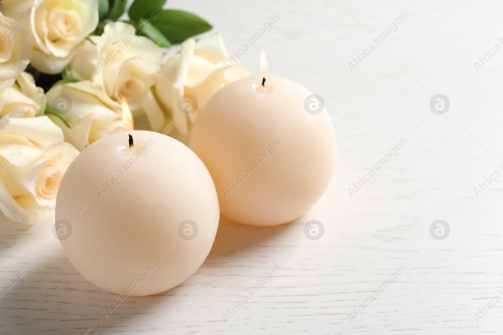 Photo of Burning wax candles and flowers on wooden table