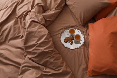 Cups of hot drink and cookies on bed with brown linens in stylish room, above view