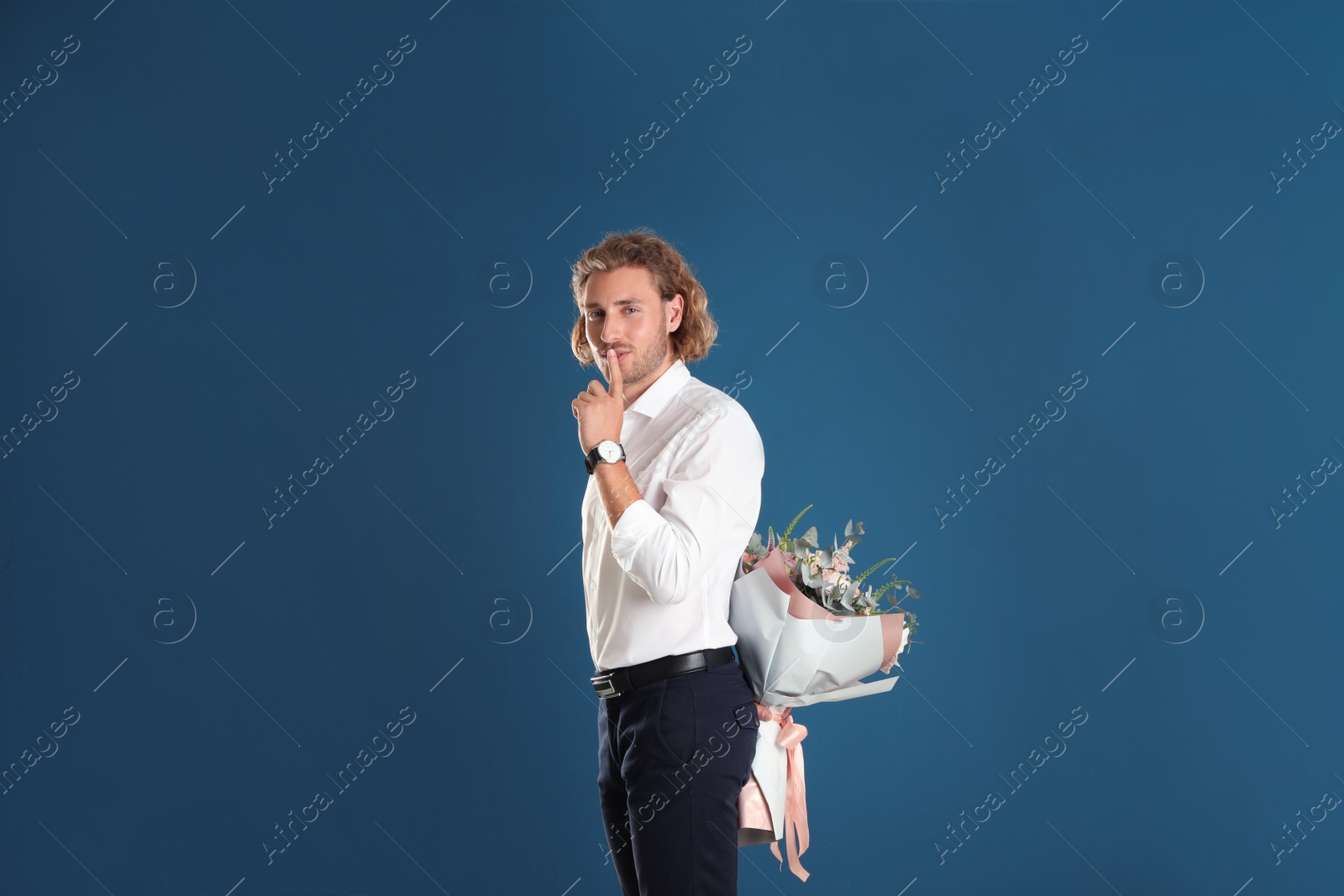 Photo of Young handsome man hiding beautiful flower bouquet behind his back on blue background