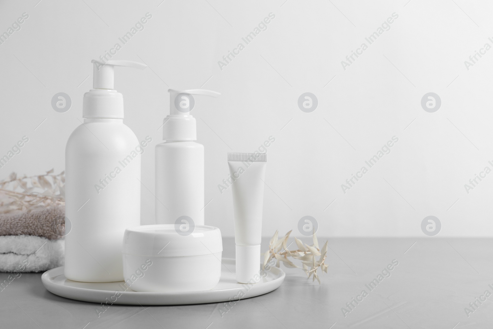 Photo of Different cosmetic products, towels and dry leaves on grey table. Space for text