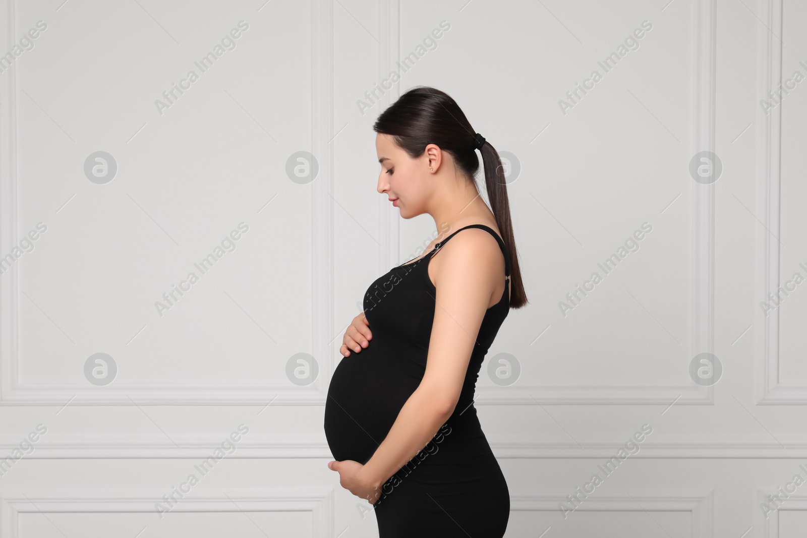 Photo of Beautiful pregnant woman in black dress near light grey wall