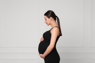 Beautiful pregnant woman in black dress near light grey wall