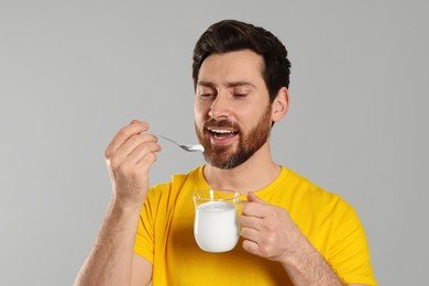 Handsome man eating delicious yogurt on light grey background