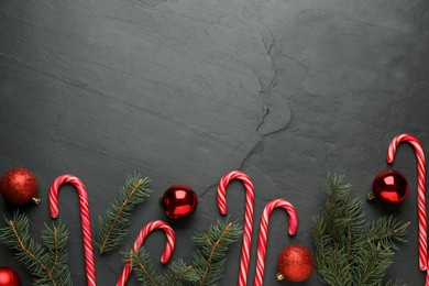 Tasty candy canes, fir branches and Christmas balls on black table, flat lay. Space for text