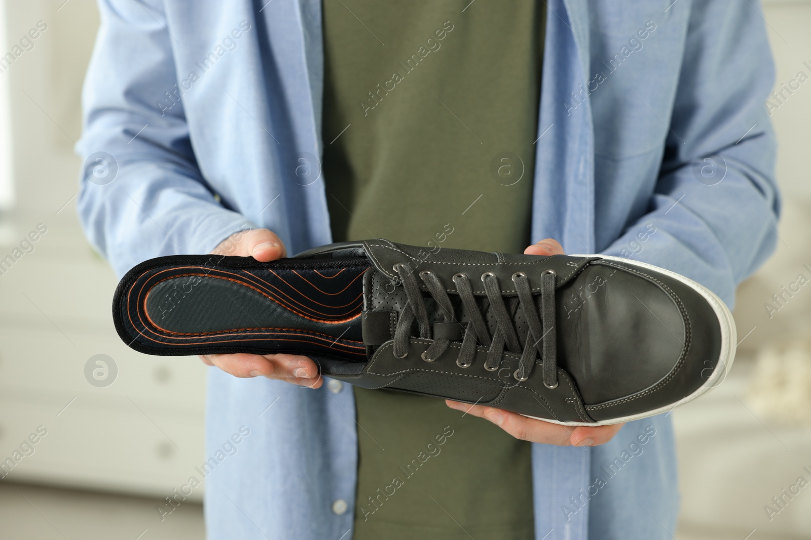 Photo of Man putting orthopedic insole into shoe indoors, closeup