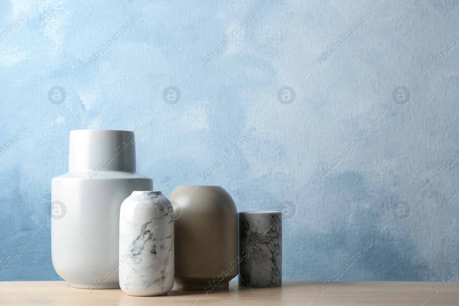 Photo of Stylish ceramic vases on wooden table against light blue background. Space for text