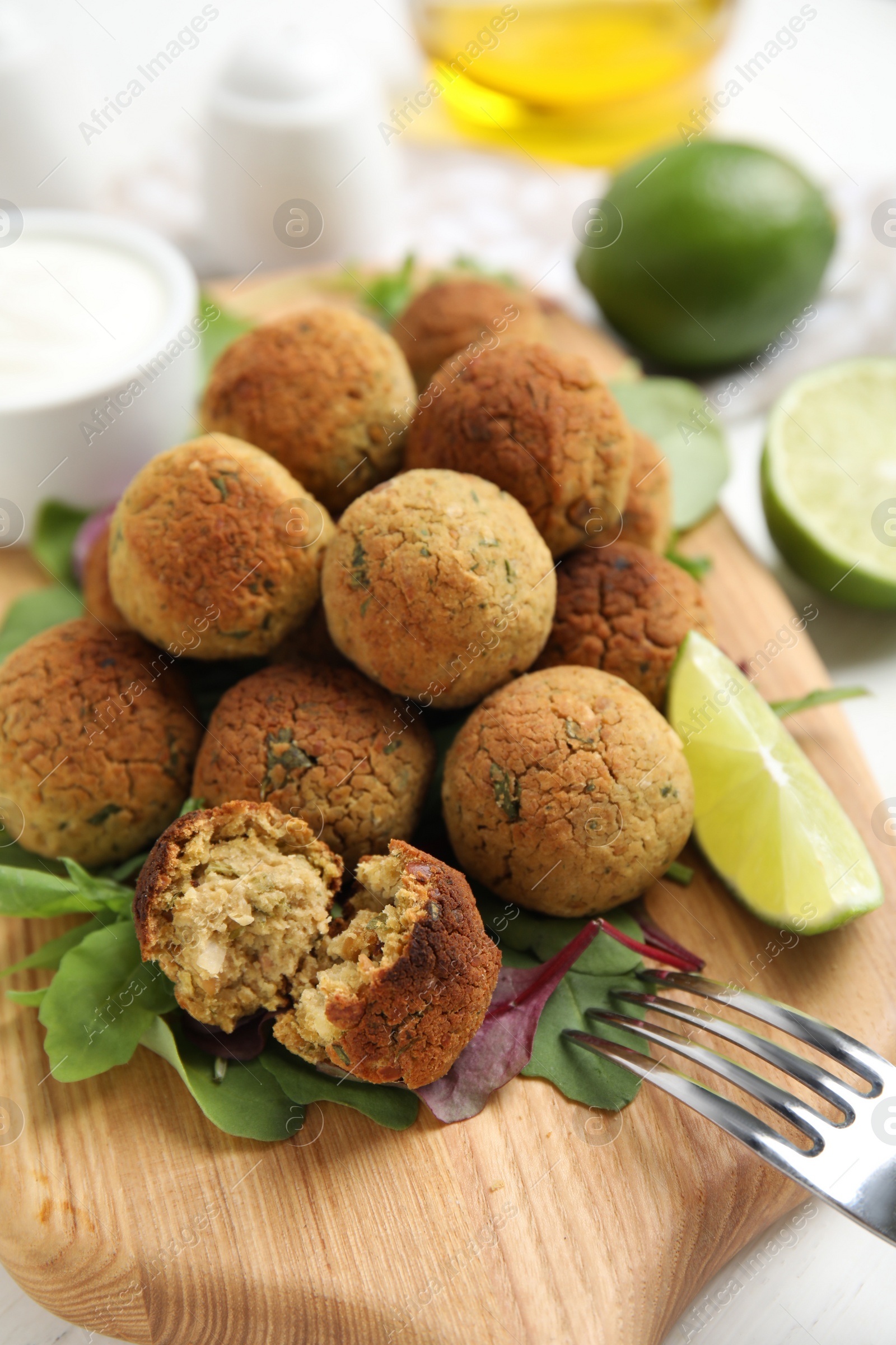 Photo of Delicious falafel balls with herbs and lime on wooden board, closeup