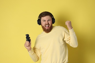 Photo of Happy man in headphones with game controller on pale yellow background