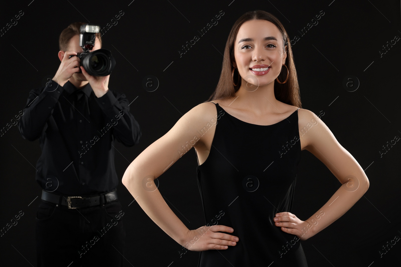 Photo of Professional photographer taking picture of beautiful young woman on black background, selective focus