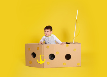 Photo of Cute little child playing with cardboard ship on yellow background