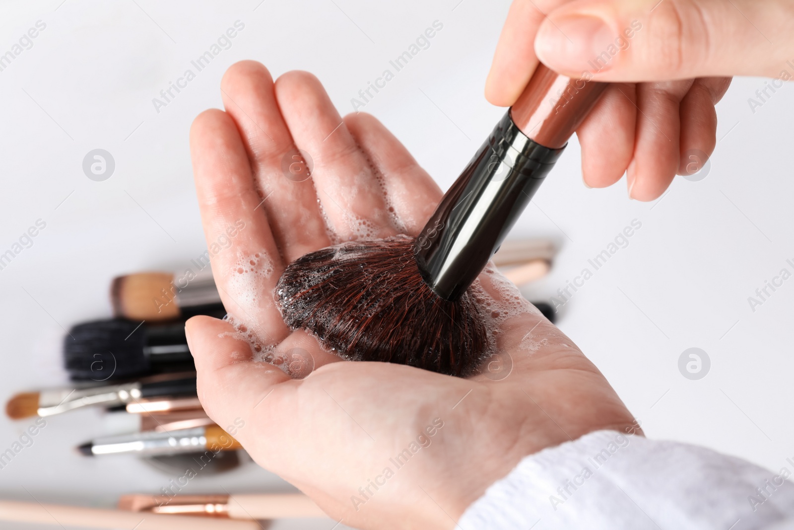 Photo of Woman washing makeup brush with soap, closeup