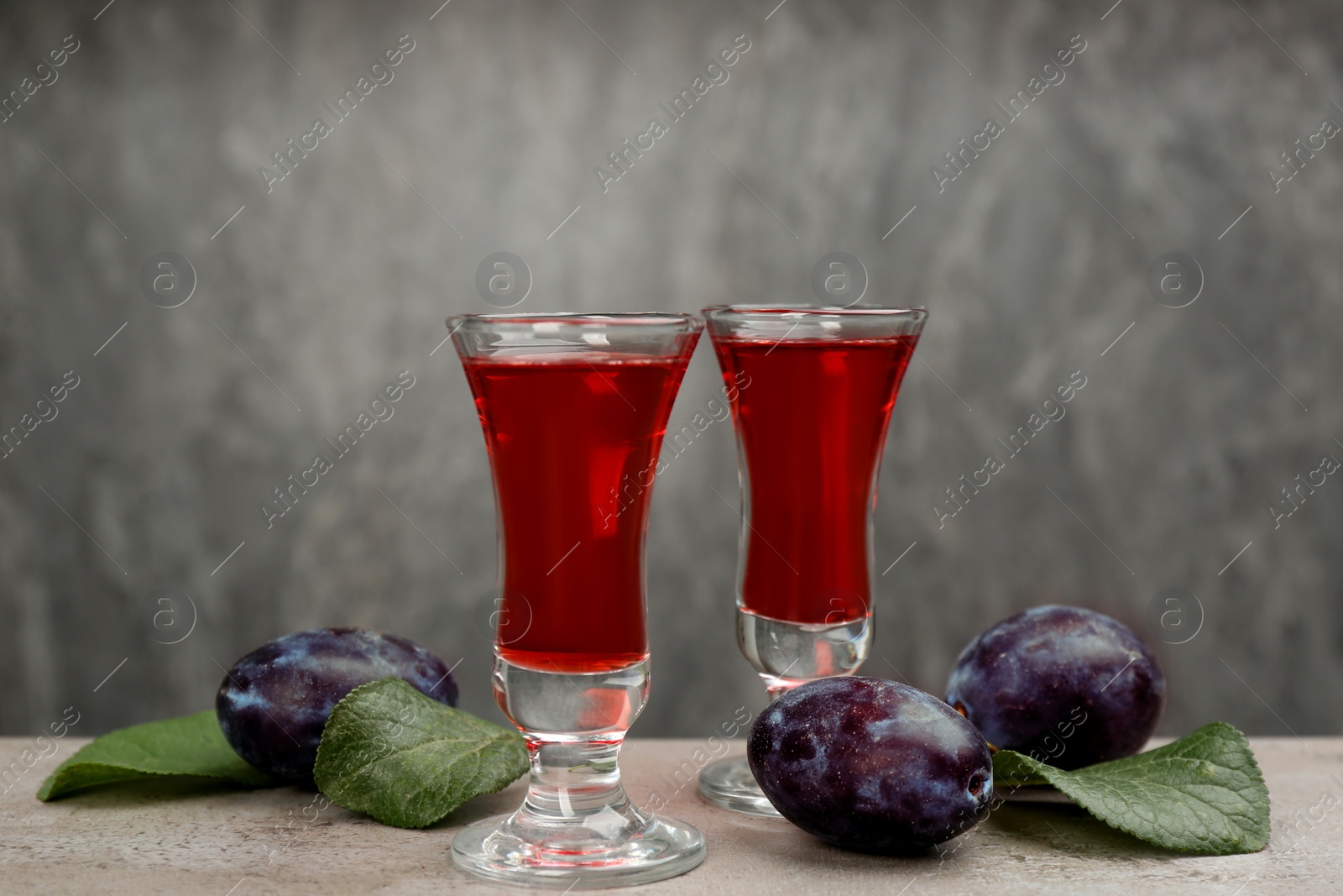 Photo of Delicious plum liquor and ripe fruits on table against grey background. Homemade strong alcoholic beverage