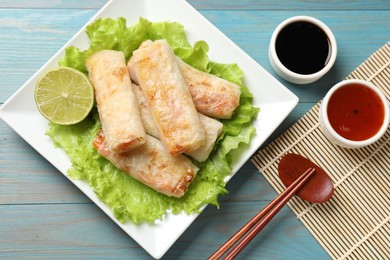 Photo of Delicious fried spring rolls served on light blue wooden table, flat lay