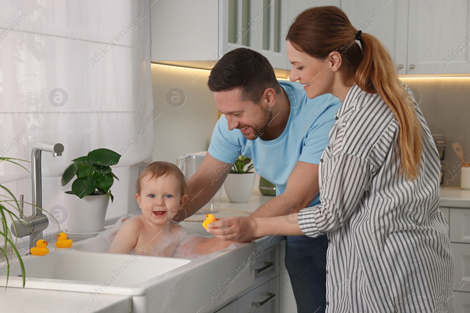 Photo of Father and mother washing their little baby in sink at home