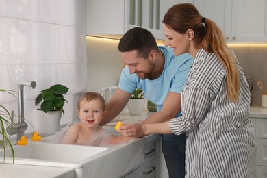 Father and mother washing their little baby in sink at home