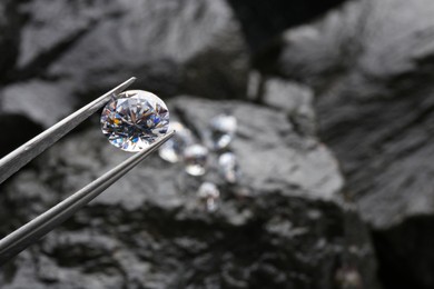 Tweezers with beautiful shiny diamond over stones, closeup. Space for text