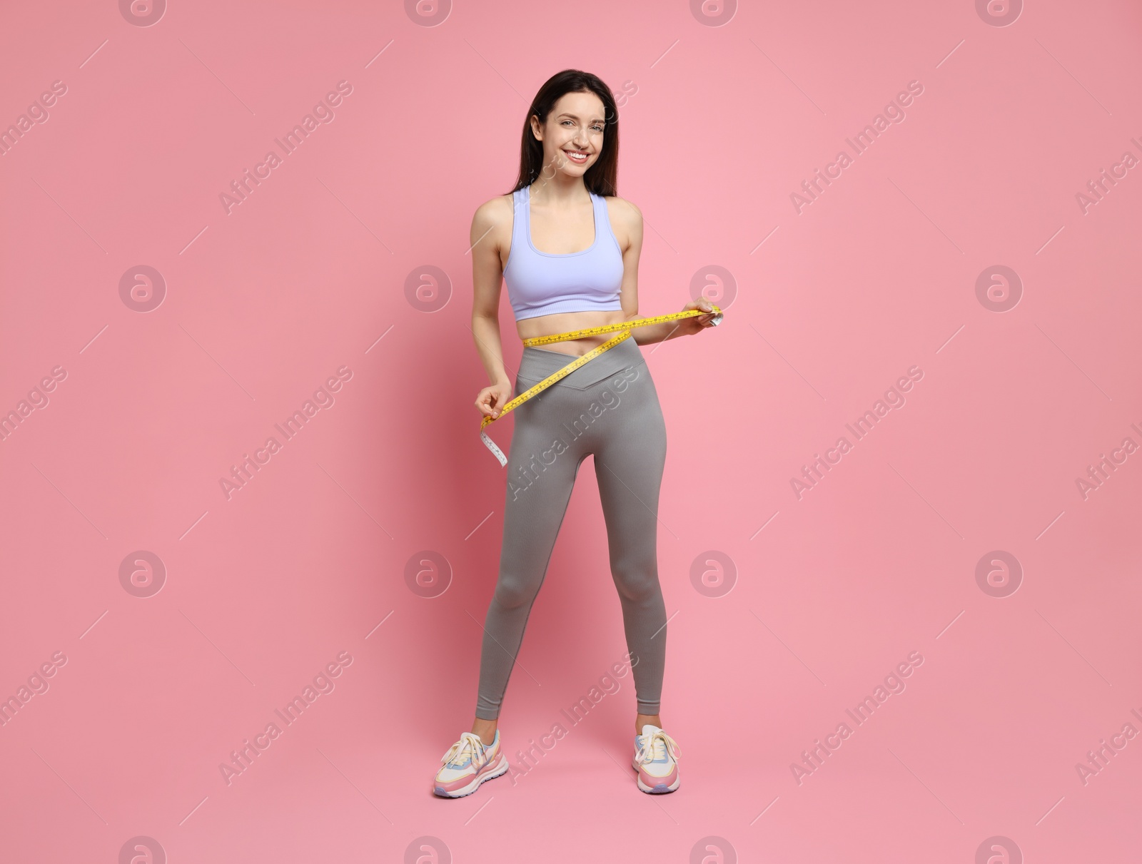 Photo of Happy young woman with measuring tape showing her slim body on pink background